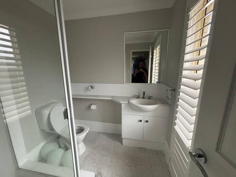 Dated bathroom with a single basin vanity, framed shower screen and plain mirror