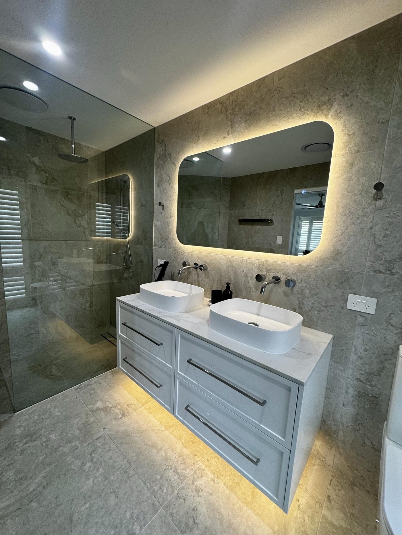 Bathroom with double vanity, walk-in shower and backlit mirror